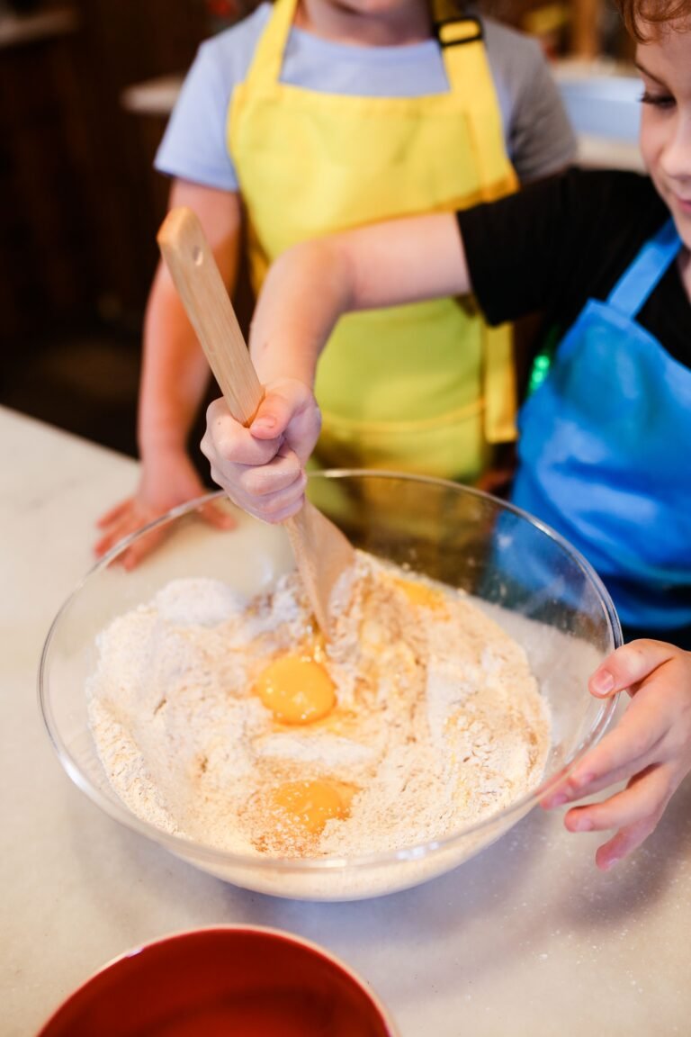 Two children in aprons enthusiastically mix ingredients in a bowl for a fun baking activity.