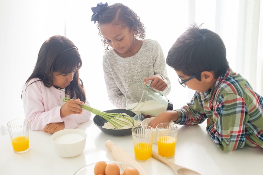 Three kids actively engaged in baking together, mixing ingredients in a bright, sunny kitchen.